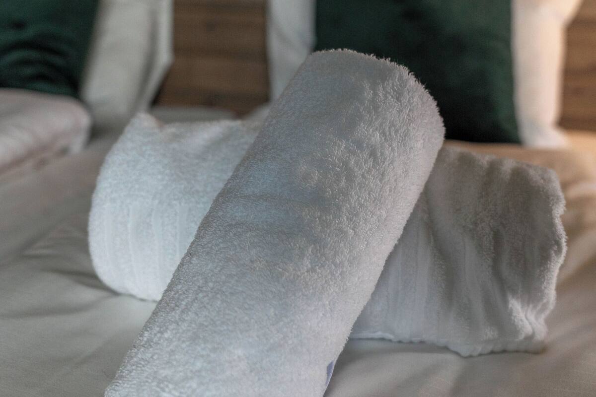 A neatly made bed with white linens and green pillows.