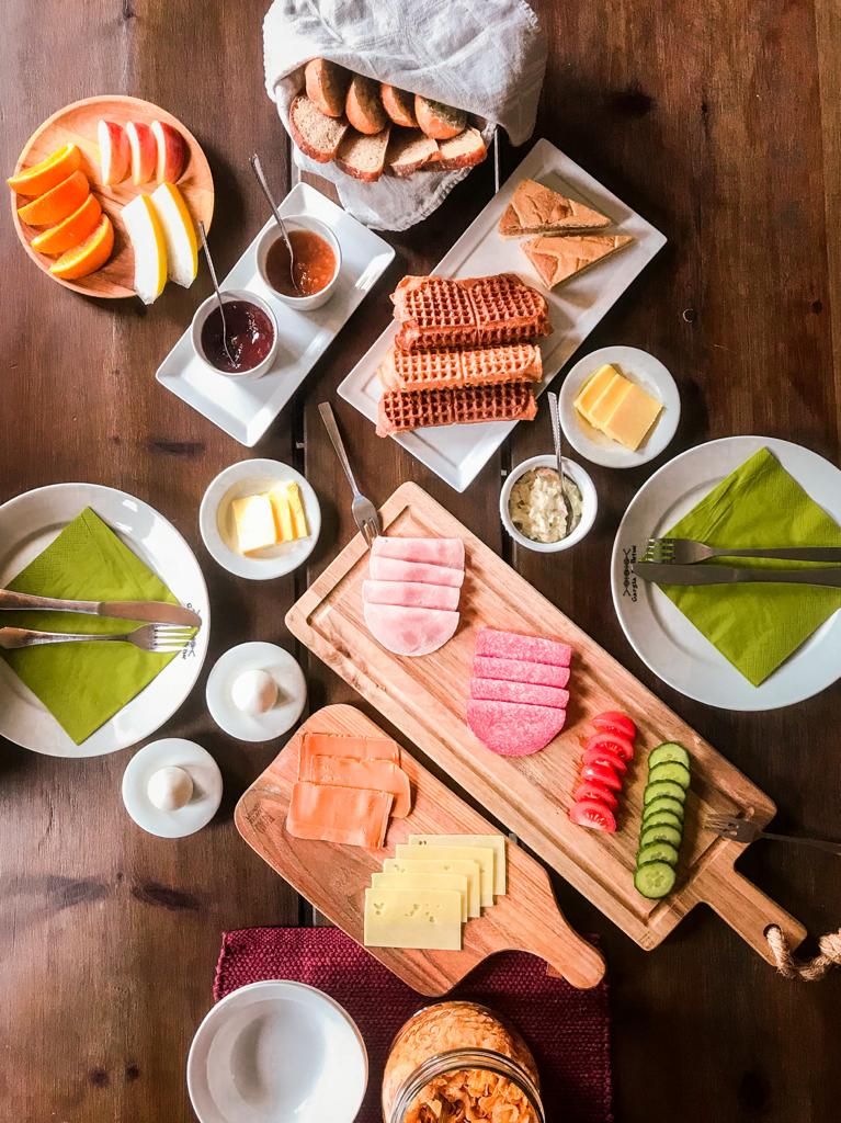 Una mesa de madera con diferentes alimentos, como frutas en rodajas, quesos y embutidos, dispuestos para una comida.