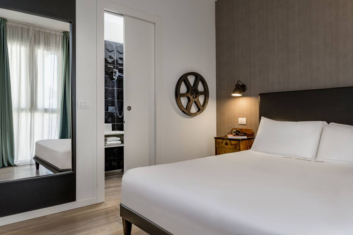 A hotel room with a bed, a nightstand, a wall clock, and a closet with shelves.