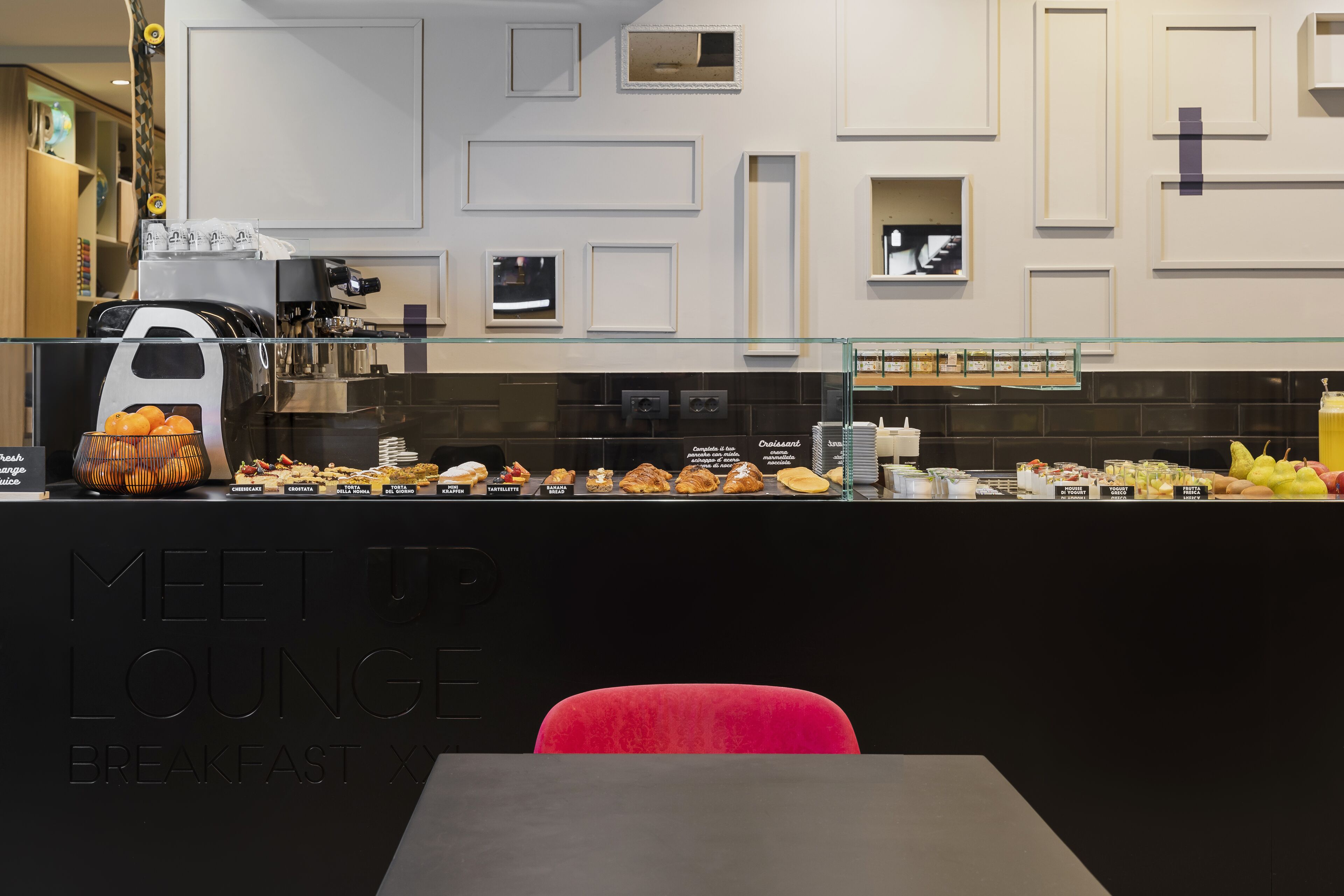 A breakfast buffet area with a variety of pastries and fruits, a coffee machine, and a glass display case.