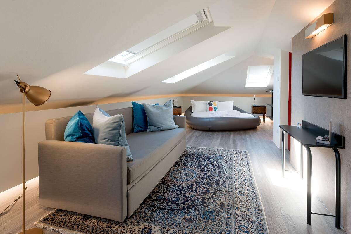 A modern loft bedroom with a sofa bed, a flat-screen TV, and a skylight.