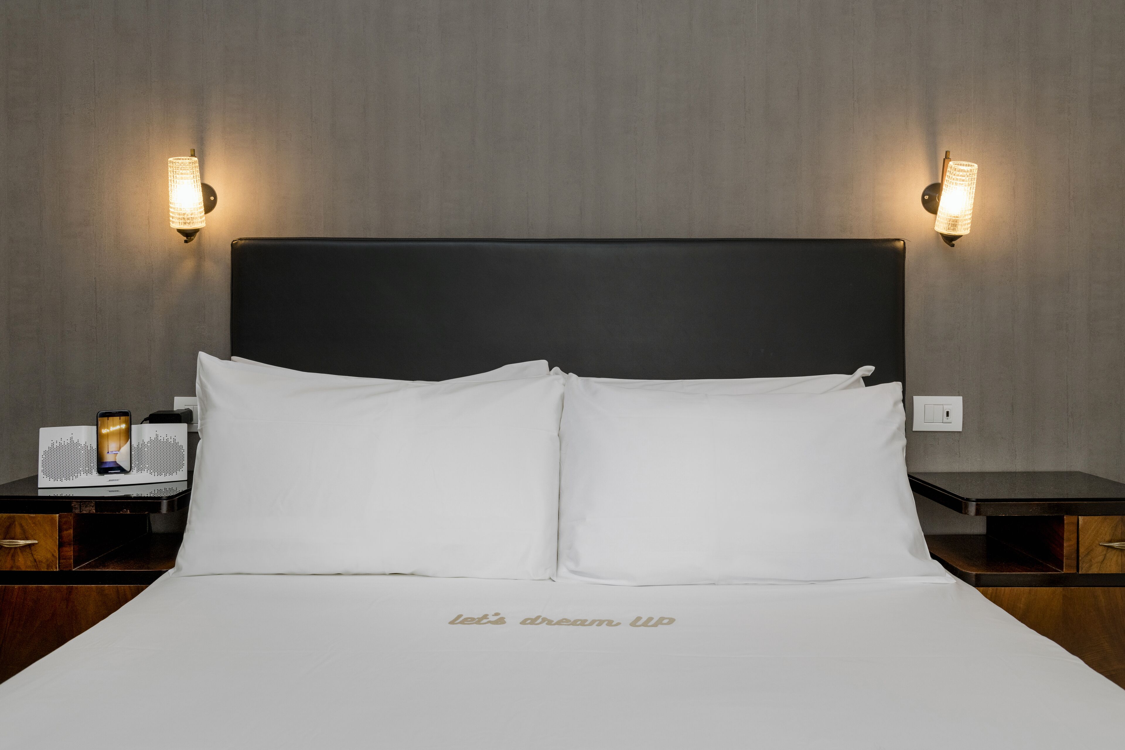A neatly made bed with white linens and a "Let's dream up" embroidered on the bedspread.