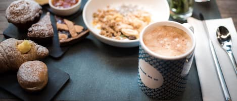 A breakfast setting with pastries, a bowl of cereal, a cup of coffee, and a glass of juice on a table.