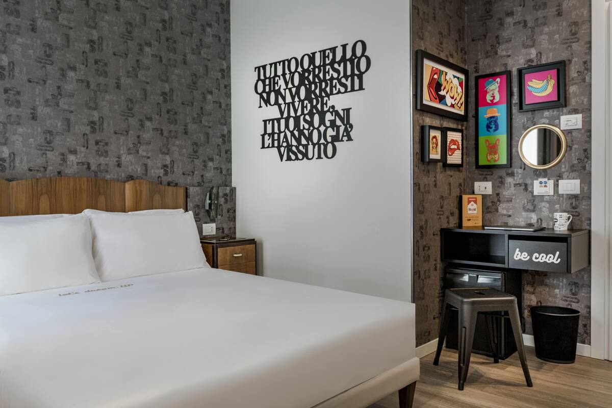 A modern bedroom with a large bed, a desk with a chair, and a wall with framed artwork.