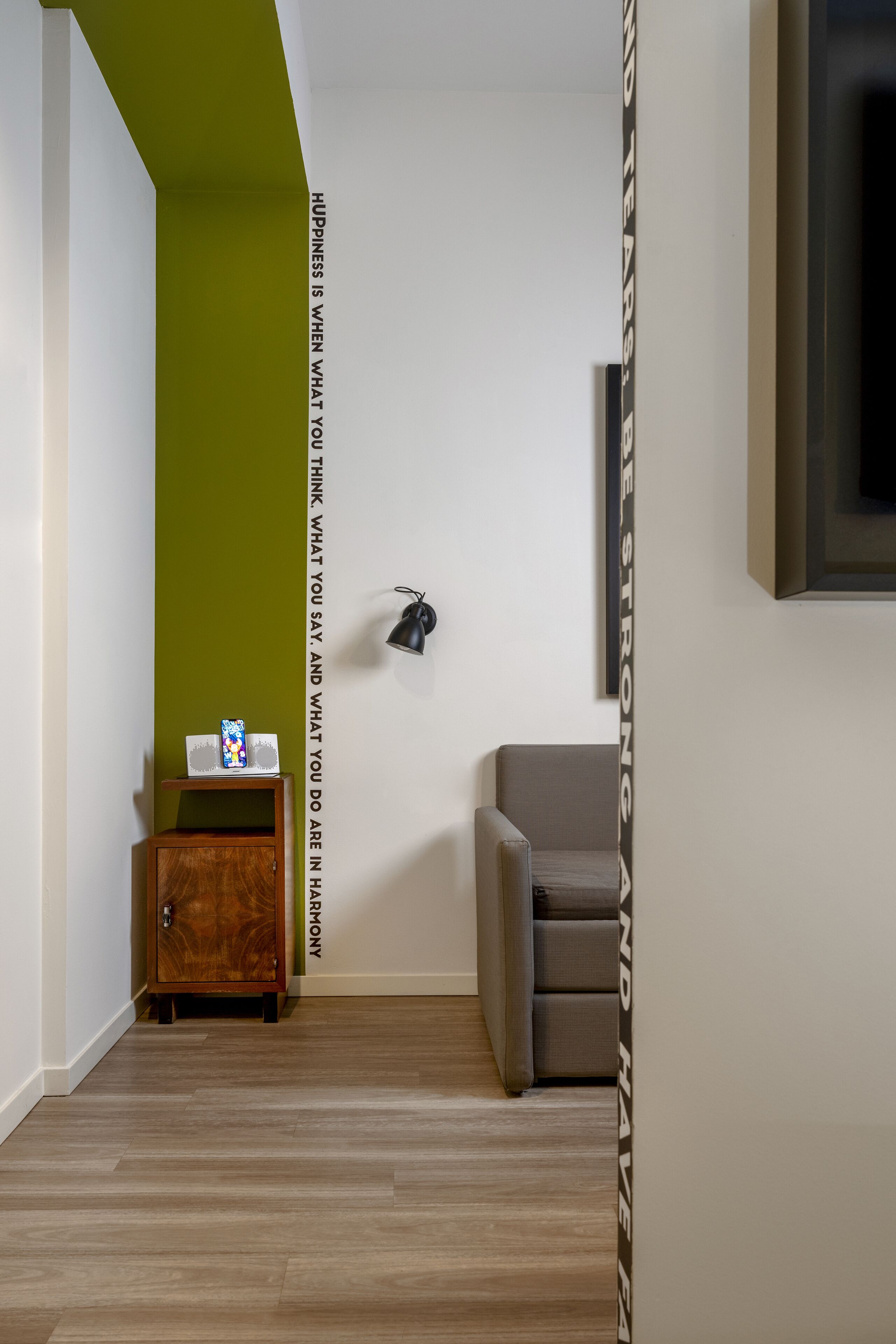 A modern room with a green accent wall, a wooden cabinet, a grey sofa, and a wall-mounted lamp.