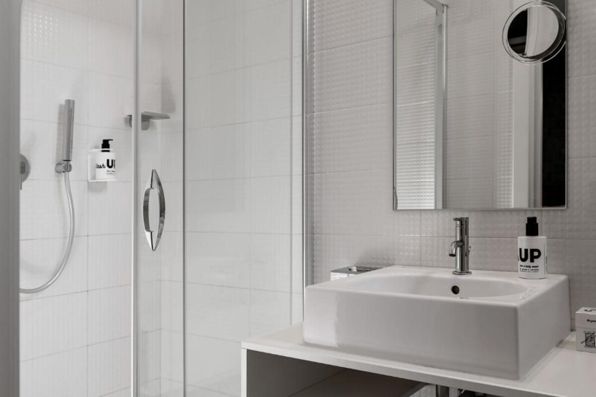 Un baño moderno con cabina de ducha de vidrio, un lavabo blanco con un espejo encima y una botella con la etiqueta 'UP' sobre el lavabo.