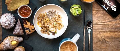 A breakfast setting with bread, pastries, a bowl of granola with fruits, a cup of coffee, a glass of orange juice, and a smartphone displaying "Start Up".