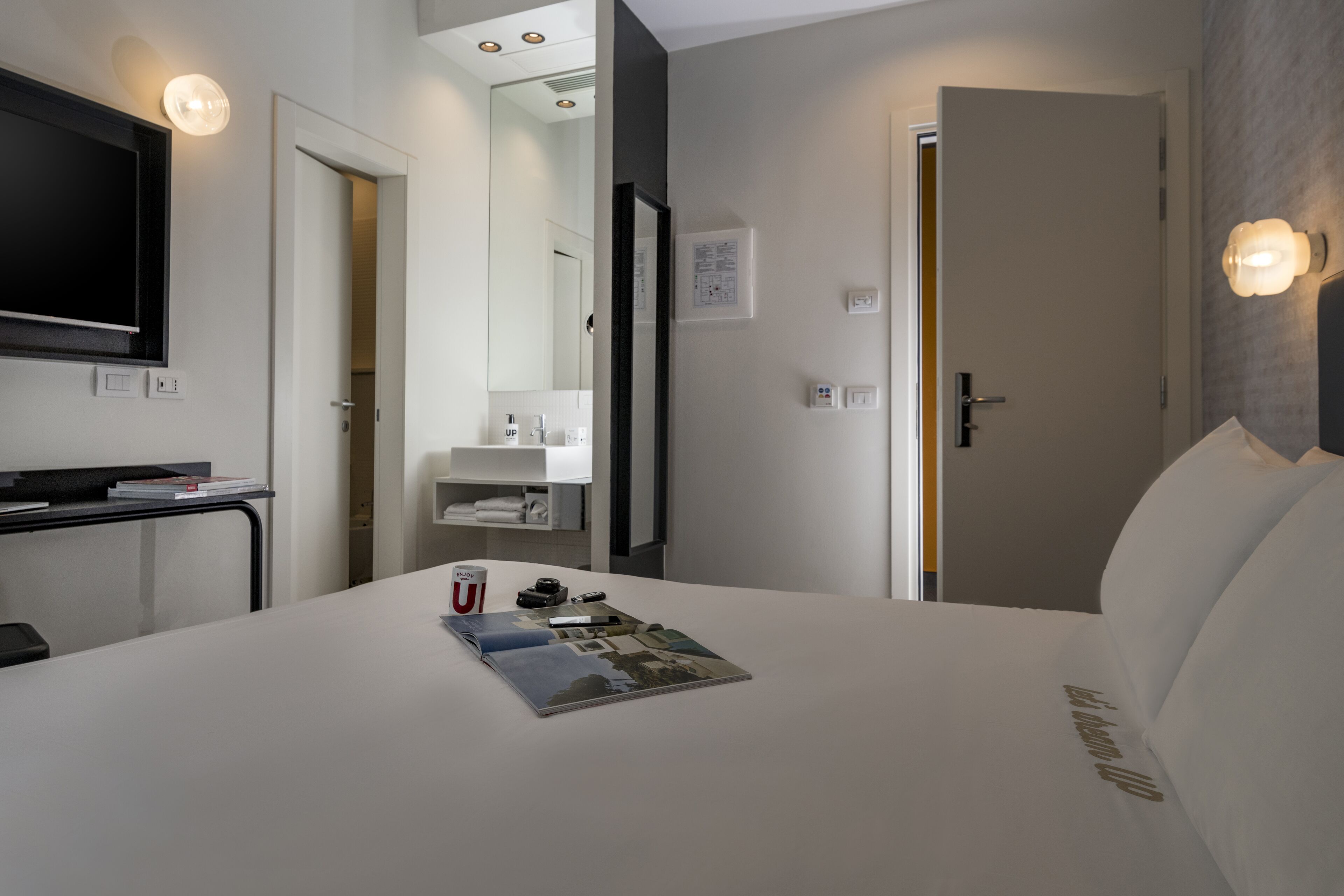 Habitación de hotel con una cama, un escritorio, un televisor y un baño visible a través de una puerta abierta.