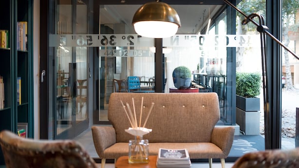 A modern interior with a sofa, a table with a vase, and a lamp. - Up Hotel (Rimini)