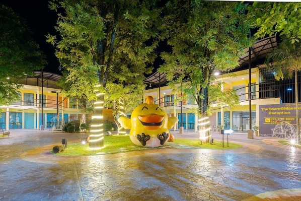 A large yellow duck sculpture in a courtyard with trees and a building labeled "The Room@Maestia Reception" in the background.