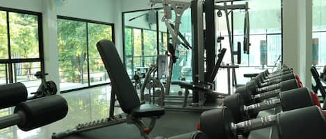 Uma academia com equipamentos de ginástica, janelas amplas e vista para árvores lá fora.