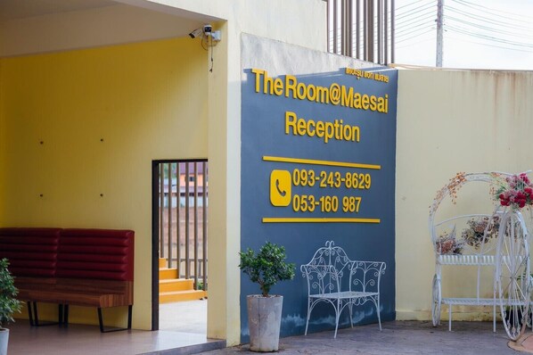 A reception area with a yellow wall, a red bench, a white metal chair, and a potted plant. - The Room at Maesai (Mae Sai)