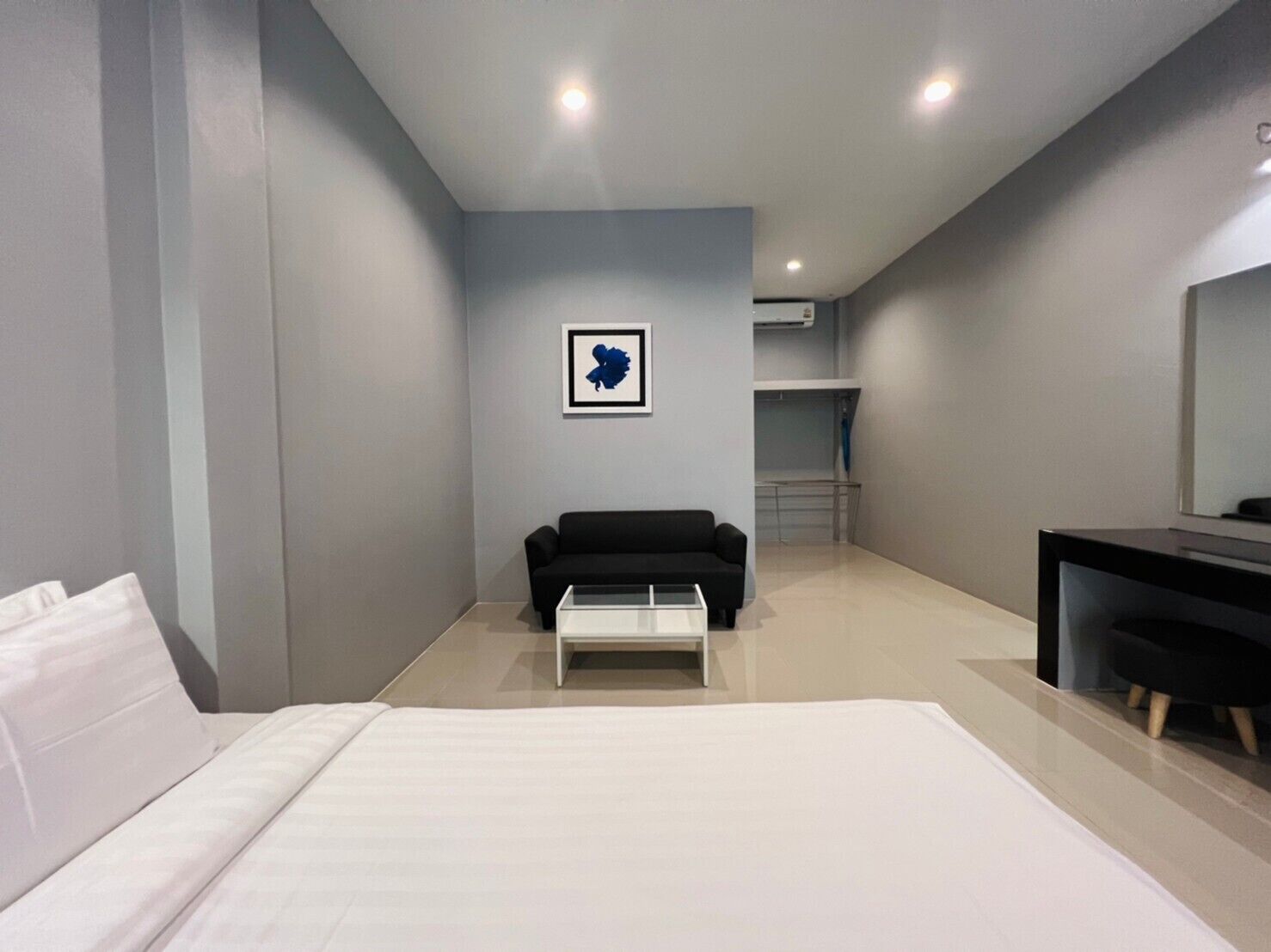 A modern hotel room with a bed, a black sofa, a small table, and a large mirror.