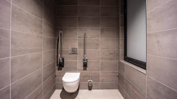 A modern bathroom with a toilet, grab bars, and a window.
