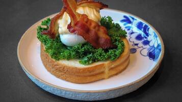 A plate with a sandwich, bacon, and a boiled egg on a ceramic plate with a blue floral pattern.