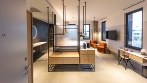 Una habitación de hotel moderna con un ventanal grande, un televisor de pantalla plana, un escritorio de madera y una zona de estar con sofá y sillones.