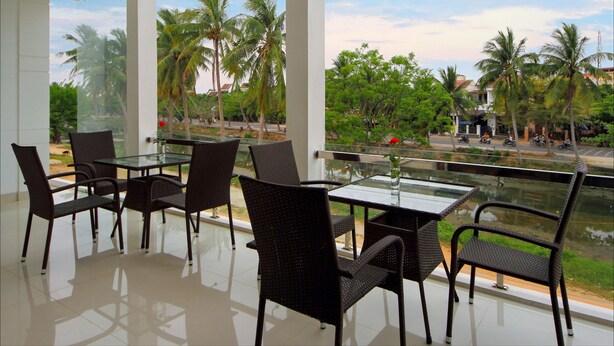 A modern outdoor dining area with glass tables and wicker chairs, overlooking a street with palm trees and a clear sky. - Azalea Homestay (Da Nang)