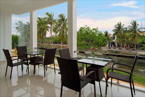 A modern outdoor dining area with glass tables and wicker chairs, overlooking a street with palm trees and a clear sky. - Azalea Homestay (Da Nang)