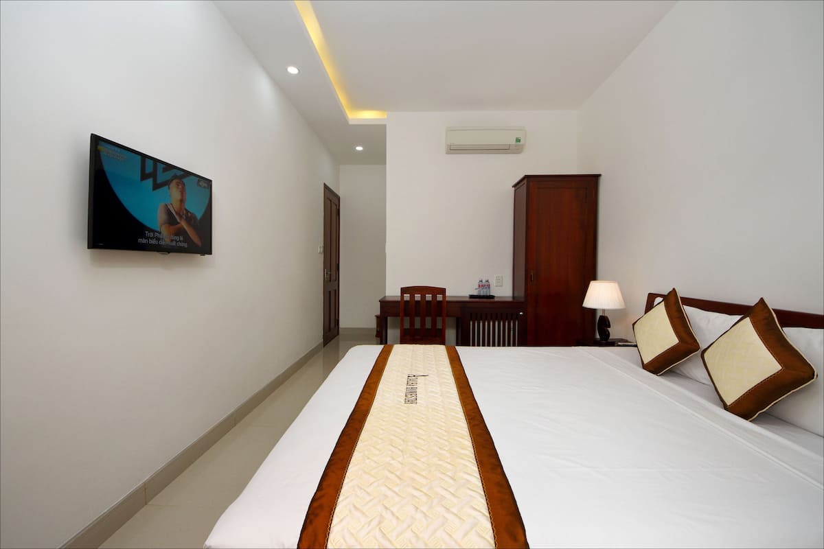 A hotel room with a bed, a desk, a chair, a lamp, and an air conditioner.