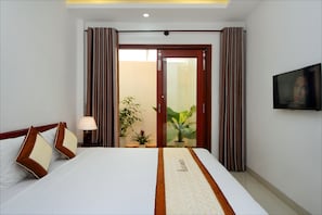 A hotel room with a bed, a TV, curtains, a potted plant, and a door leading to a balcony. - Azalea Homestay (Da Nang)