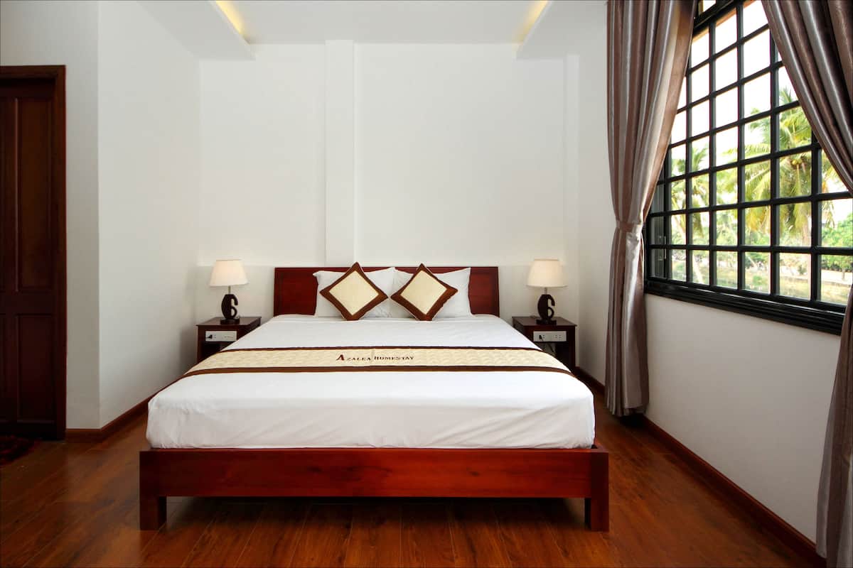 A hotel room with a wooden bed, white walls, and a window with curtains.