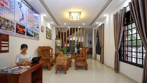 A reception area with a desk, chairs, a statue, and a large window with curtains. - Azalea Homestay (Da Nang)