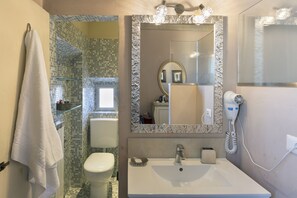 Ein Badezimmer mit Duschkabine aus Glas, Toilette, Waschbecken mit Spiegel und einem Wandhaartrockner.