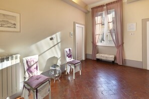 Ein Zimmer mit zwei Stühlen, einem kleinen Tisch, einer Bank, einem Heizkörper und einem Fenster mit Vorhängen.