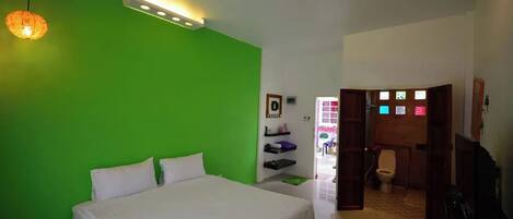 A bedroom with a green wall, a bed with white bedding, a hanging light fixture, and a door leading to a bathroom.