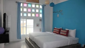 Un dormitorio con cama, cortinas, una lámpara de pared y una ventana con motivos cuadrados de colores.