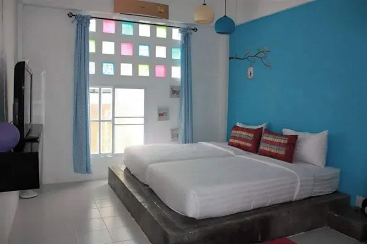 A bedroom with a bed, curtains, a wall-mounted lamp, and a window with colorful square patterns.