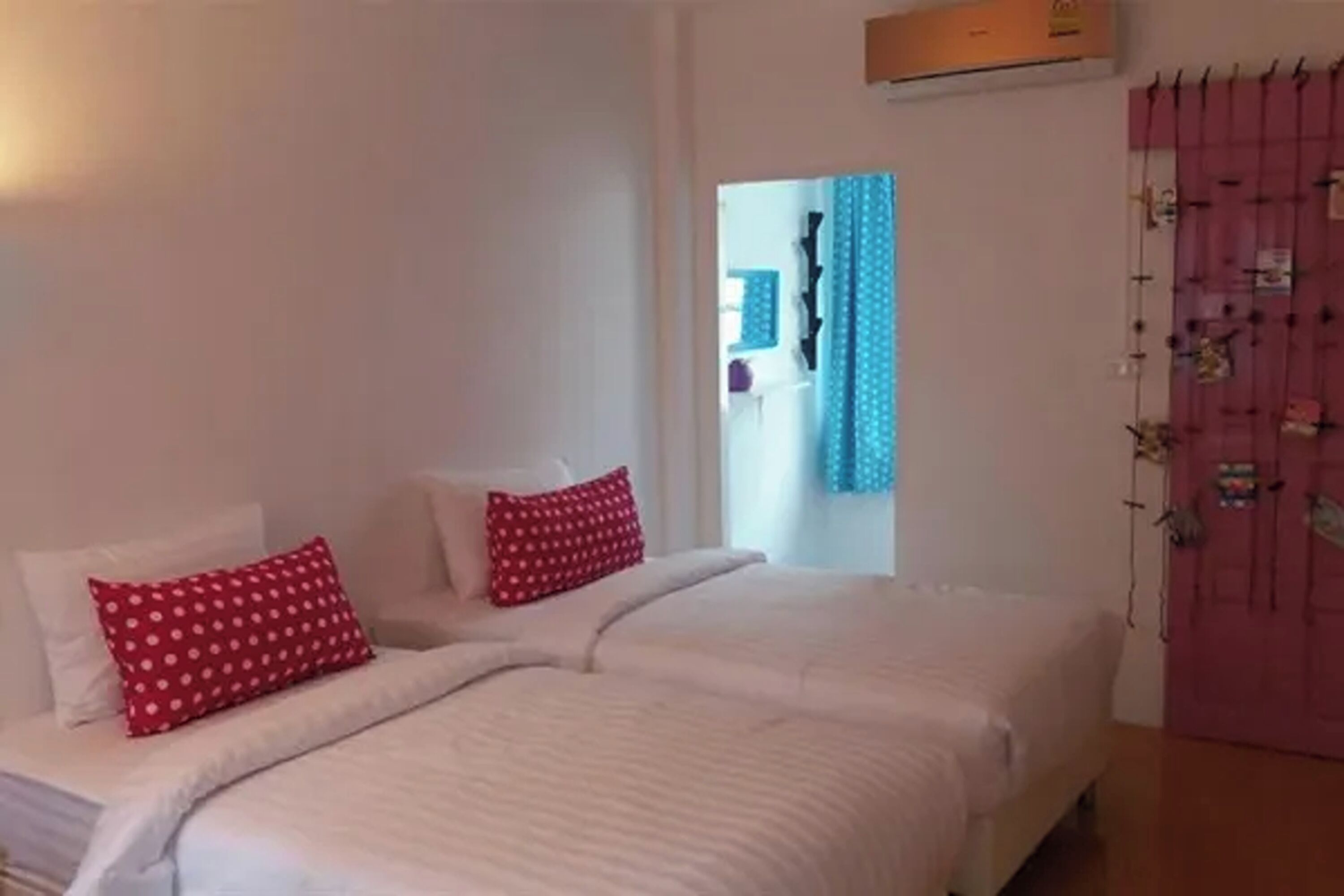 A bedroom with a bed, two pillows, a window with curtains, and a wall-mounted air conditioning unit.
