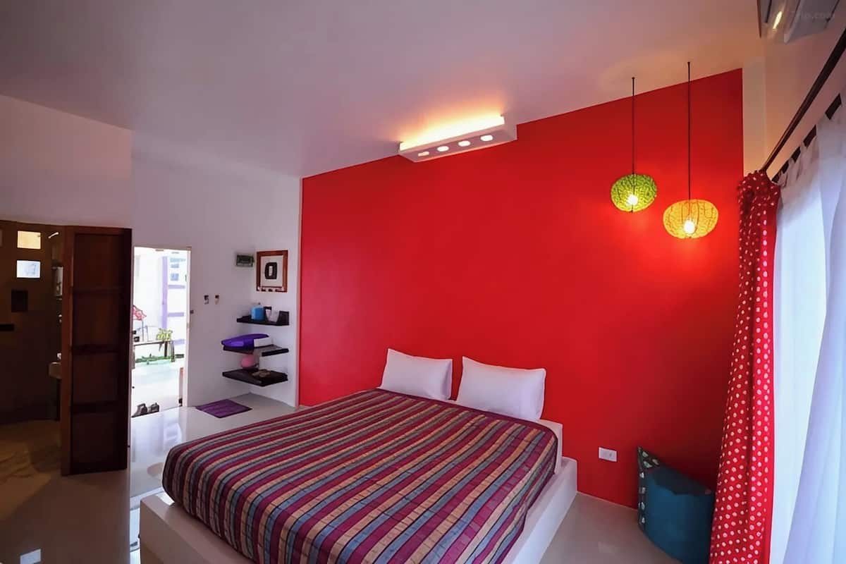 A modern bedroom with a red accent wall, a striped bedspread, and a ceiling light fixture.
