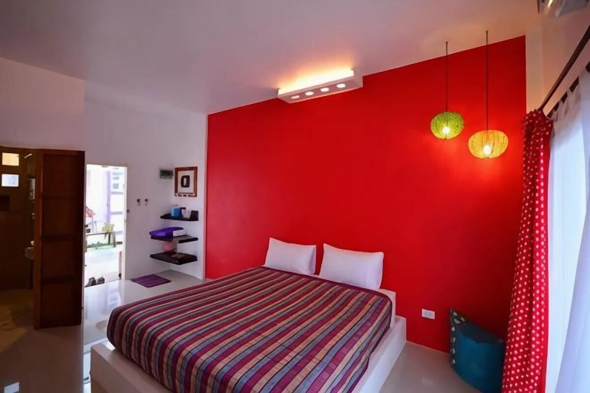 A bedroom with a red accent wall, a striped bedspread, and a ceiling light fixture.