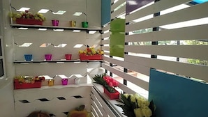Una habitación con paredes de listones blancos, varias estanterías con coloridas exhibiciones de flores y vistas al verdor del exterior.