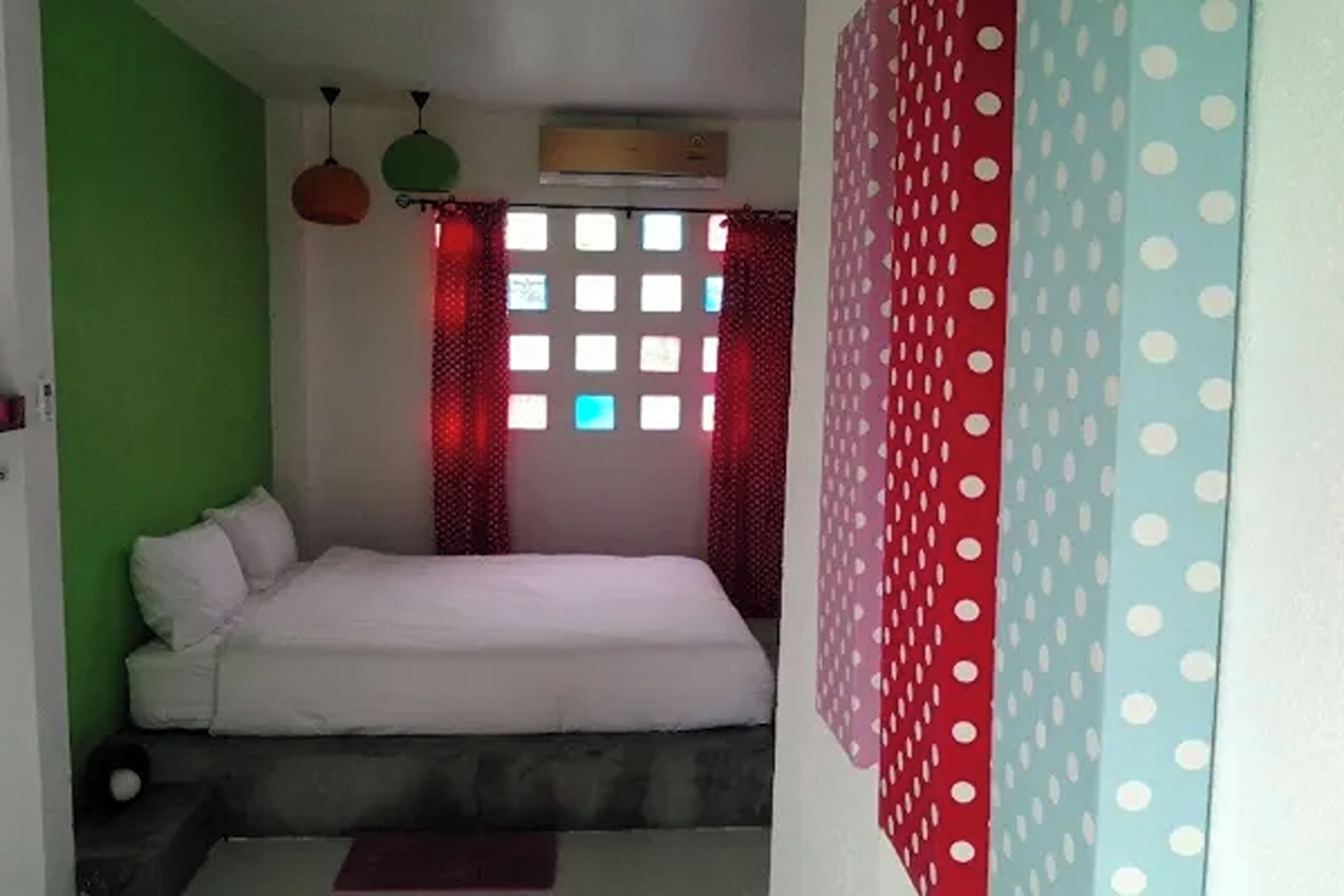 A bedroom with a bed, a window with red curtains, and an air conditioning unit on the wall.