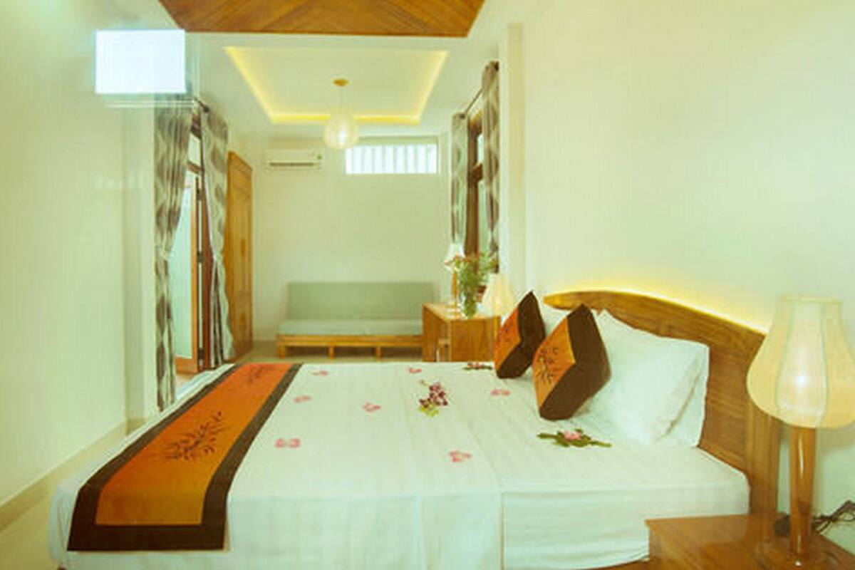 A hotel room with a bed, a bedside table, a lamp, and a window.