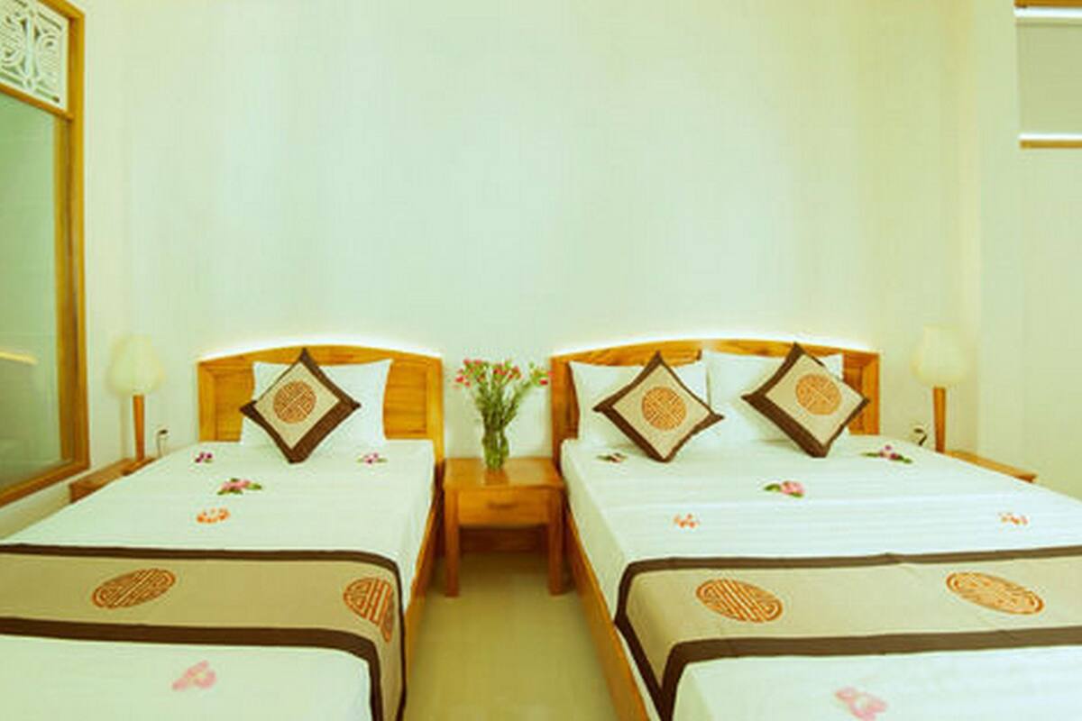 A hotel room with two single beds, each with a wooden headboard, a nightstand, and a bedside table.