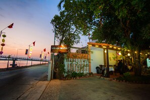 A restaurant with a signboard, outdoor seating, and a view of a bridge. - Riverside Plum Garden Homestay (Da Nang)