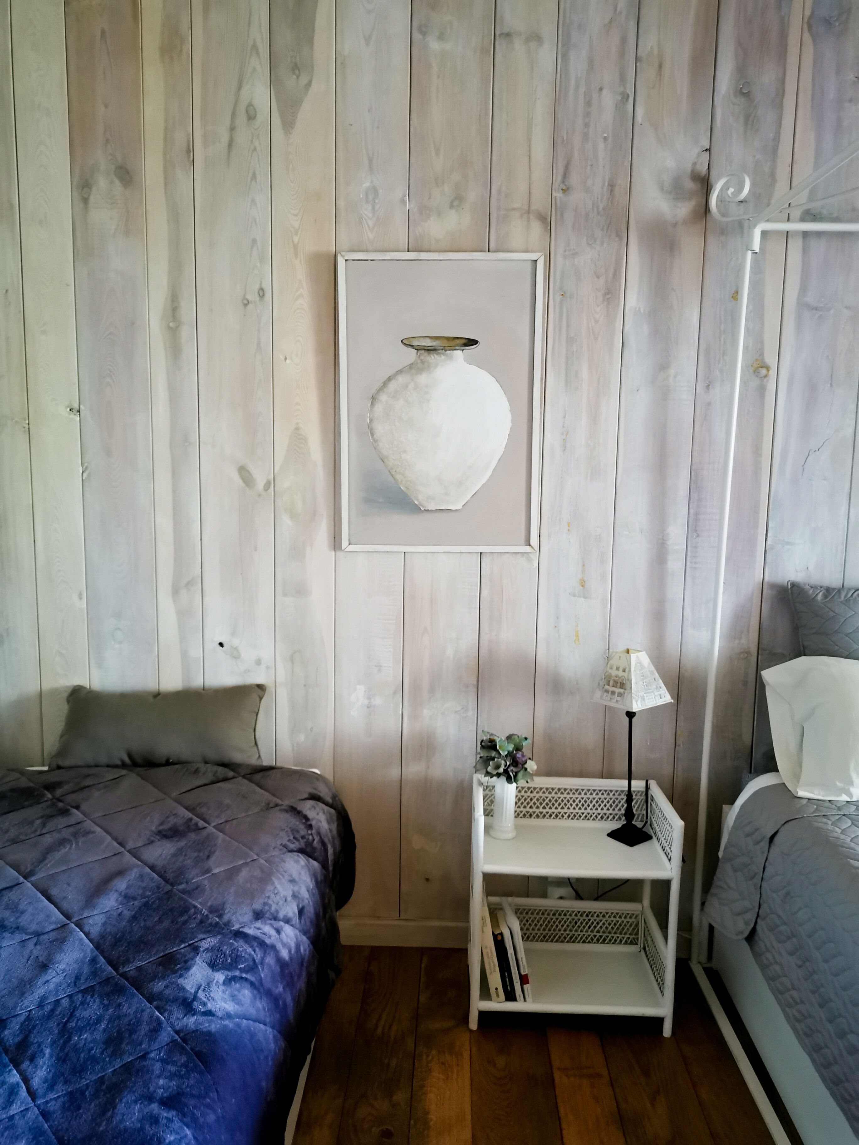 A bedroom with two beds, a nightstand with a lamp, and a framed artwork on the wall.