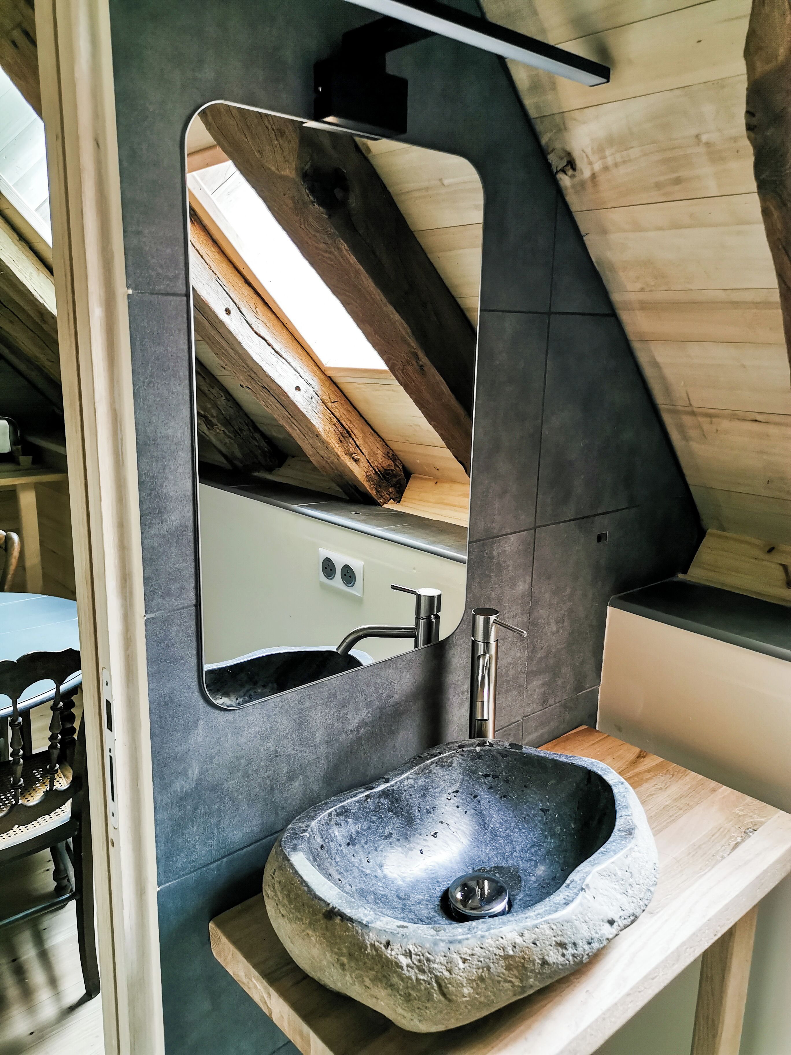 Een badkamer met een stenen wastafel, een spiegel en een houten plafond.