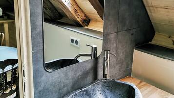 Een badkamer met een stenen wastafel, een spiegel en een houten plafond.