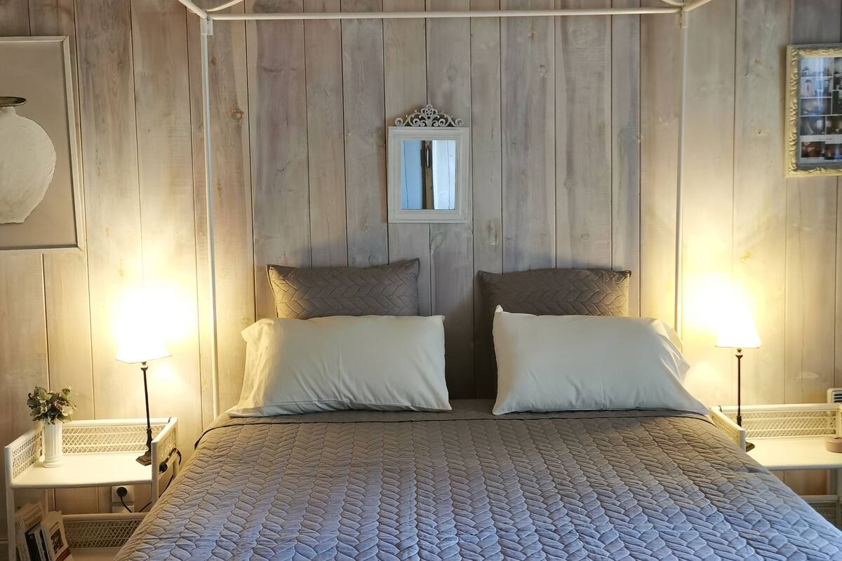 Une chambre à coucher avec une tête de lit en bois, deux tables de chevet avec des lampes, un lit recouvert d’une courtepointe à motifs et un miroir accroché au mur.
