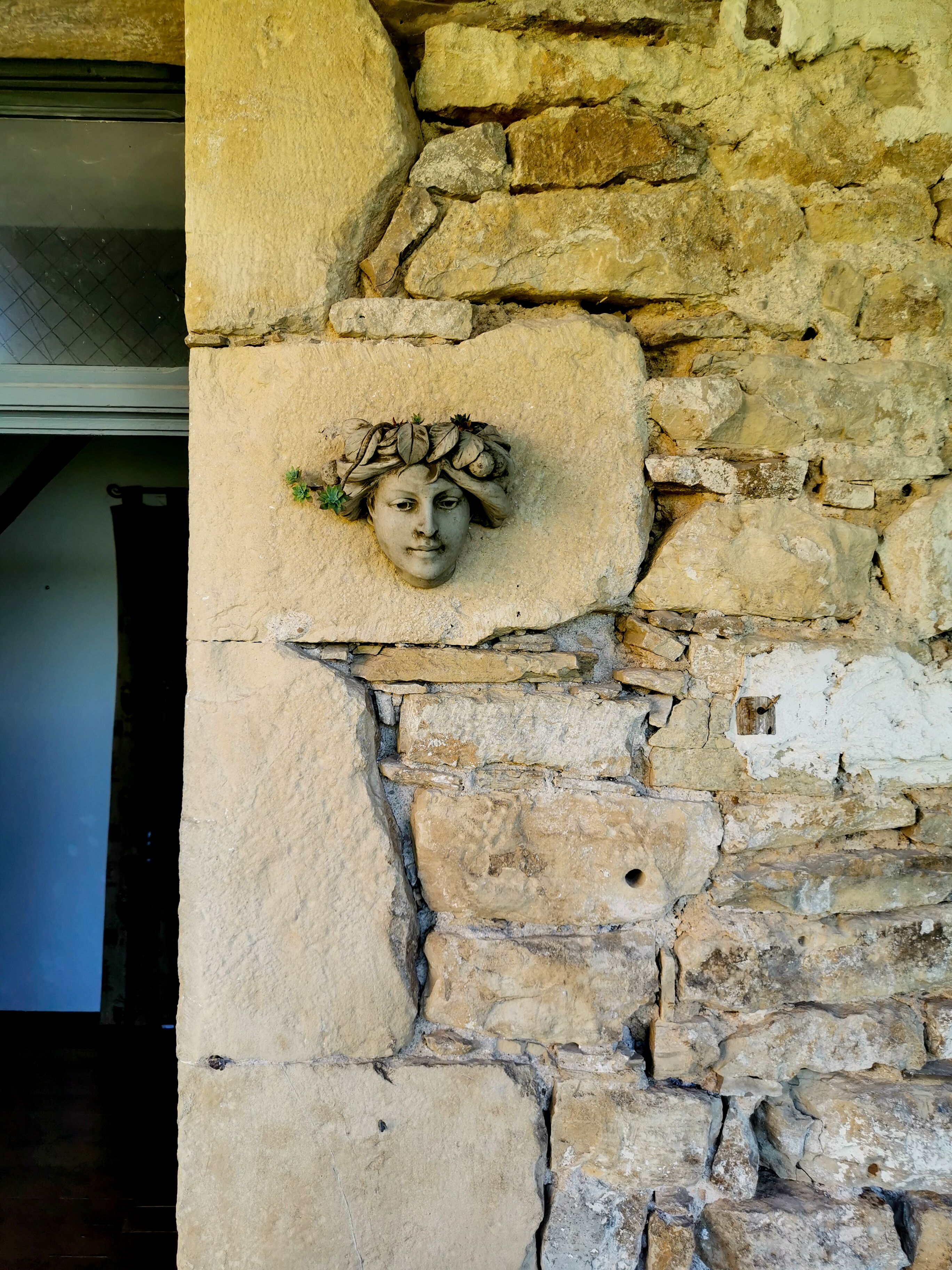 Un mur de pierre orné d’une sculpture représentant une tête.