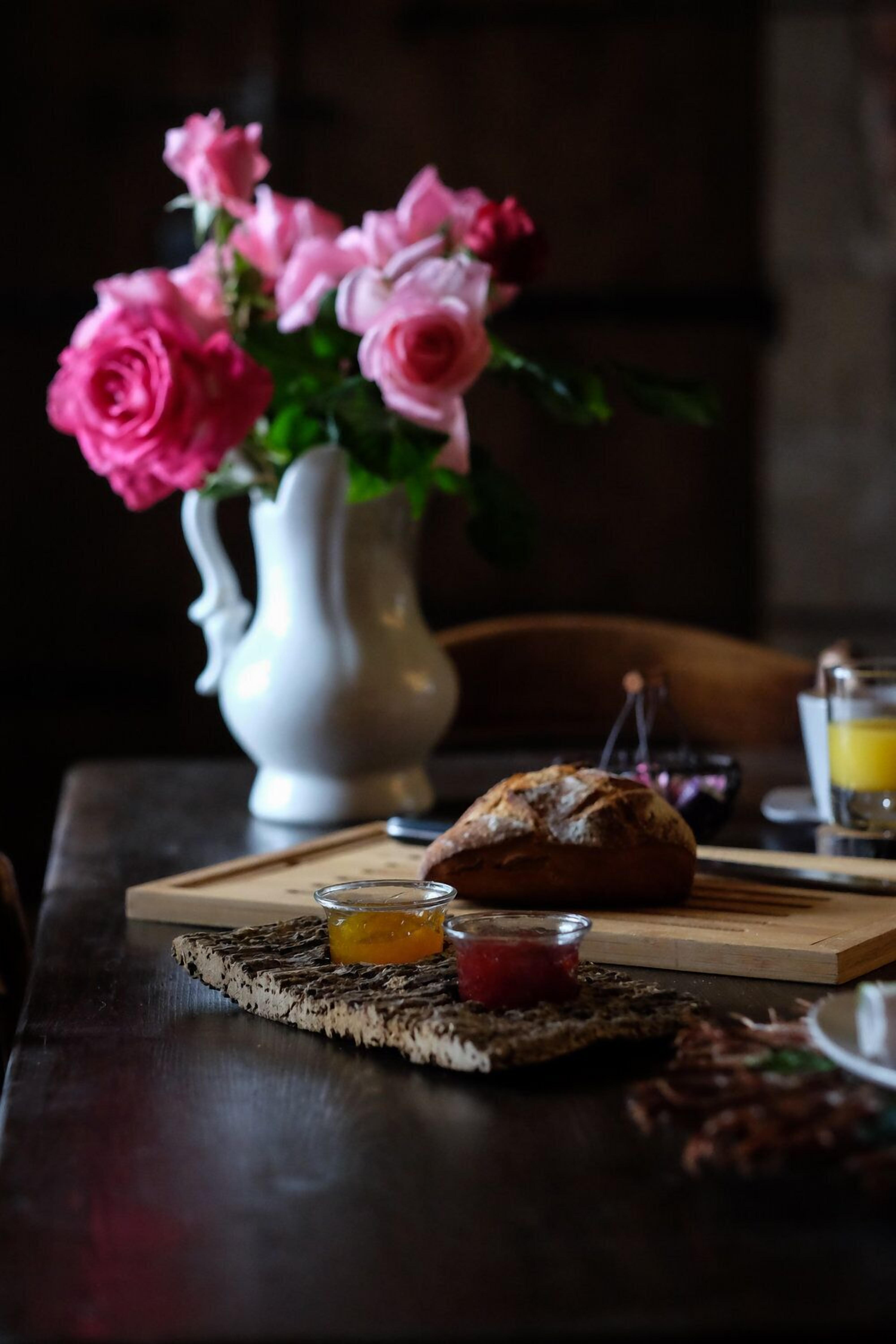 A table with a loaf of bread, a small glass of orange juice, and a jar of jam.