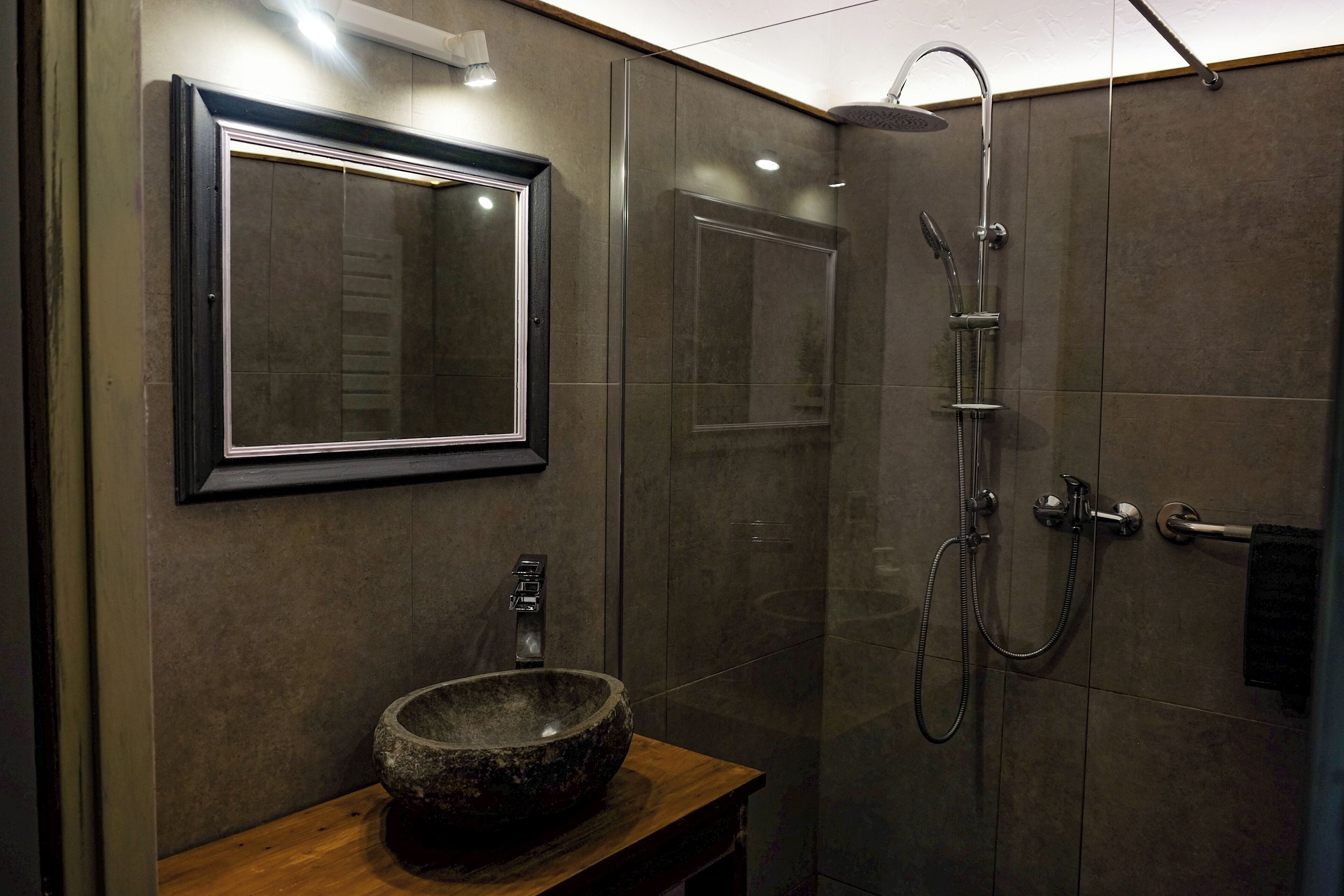 Un baño moderno con un lavamanos de piedra, un espejo grande y una ducha a ras de suelo.