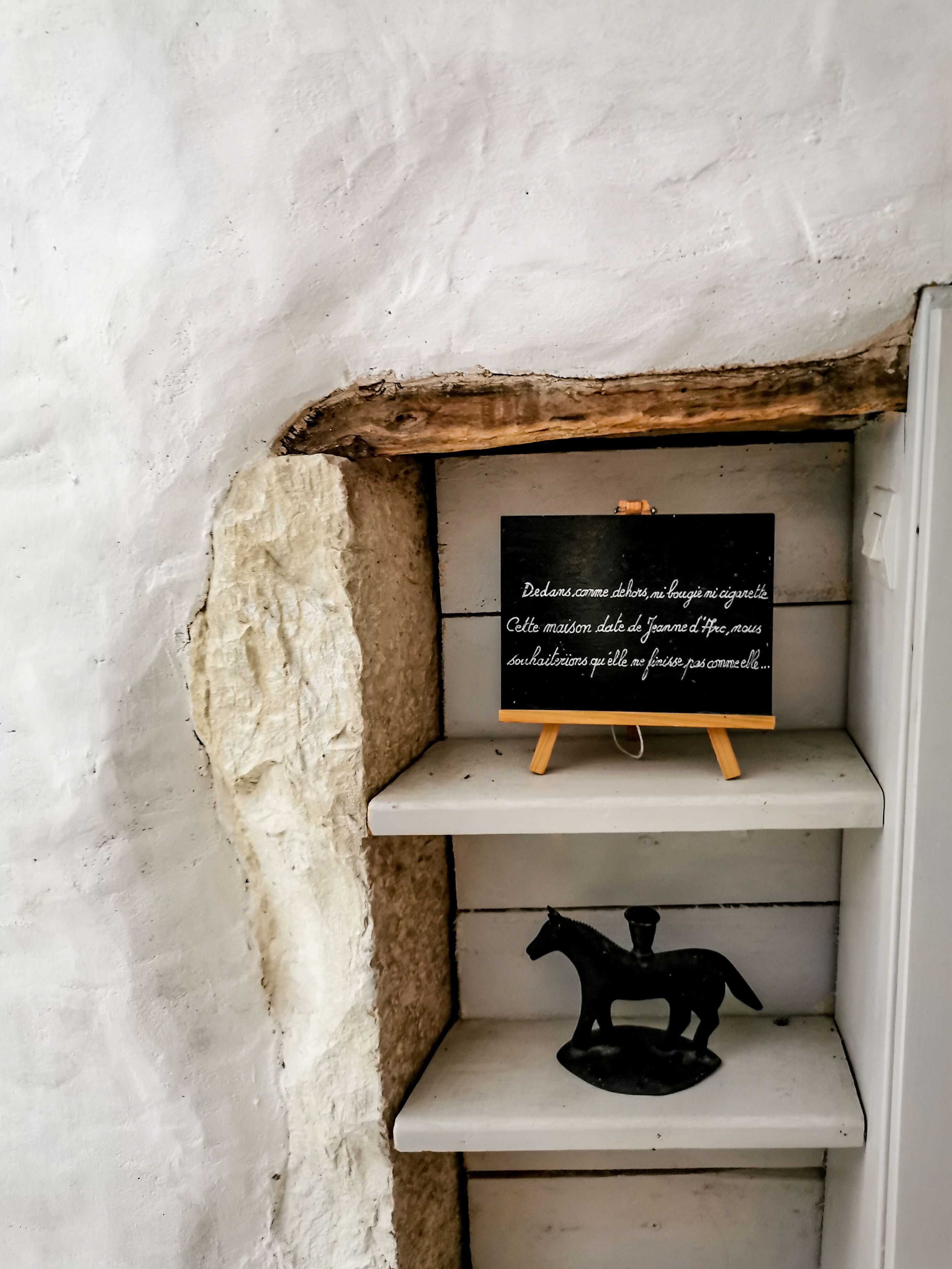 A rustic wall with a shelf holding a blackboard with French text and a black horse figurine.