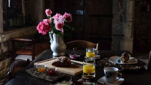 Ein Esstisch, gedeckt mit einer Vase voller rosa Blumen, einer Speisenplatte, Gläsern Orangensaft und einer rustikalen Steinwand im Hintergrund.