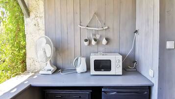 Una cocina compacta con una pared de madera, un ventilador blanco, una tetera blanca y un microondas blanco.