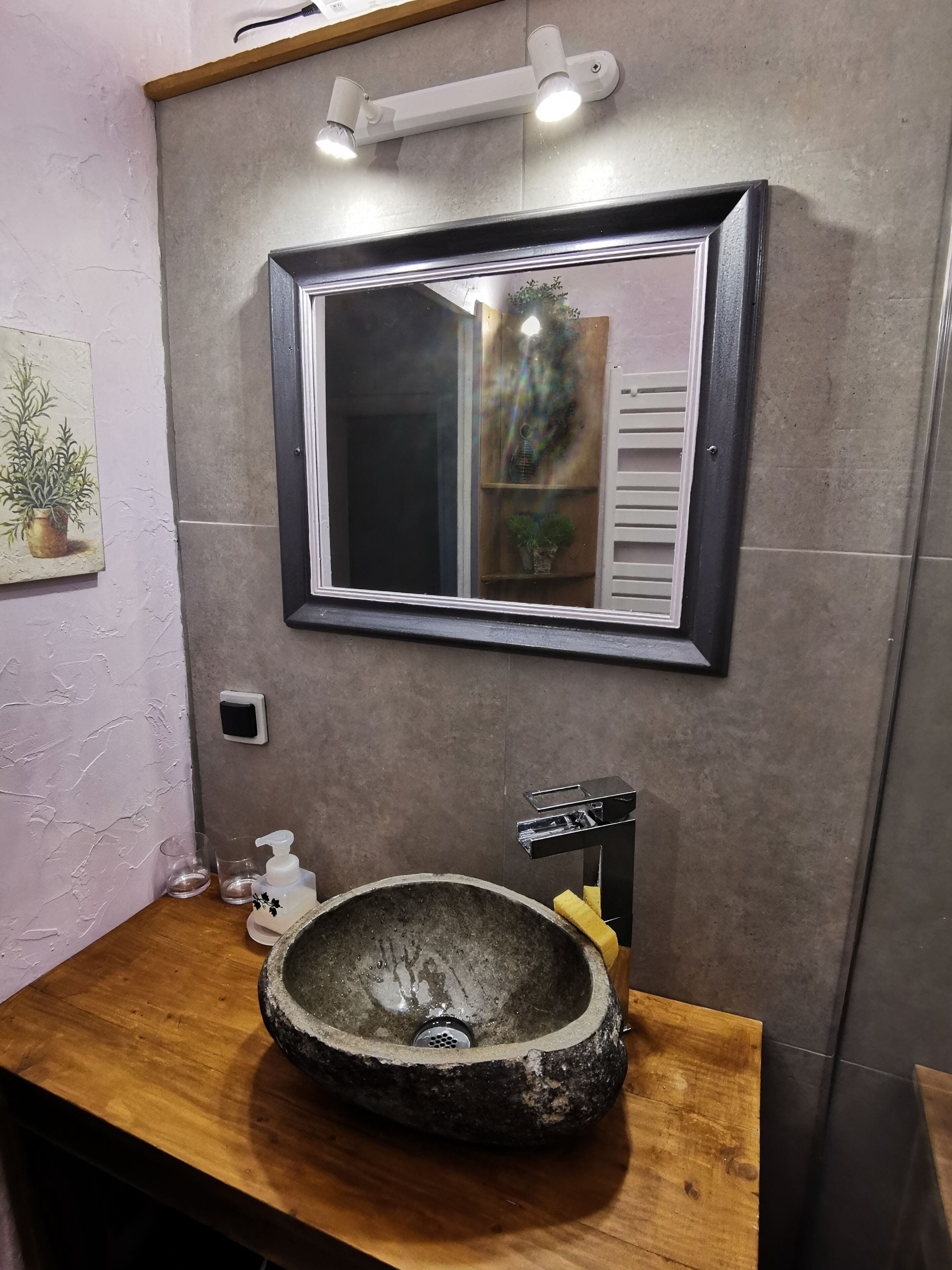 A bathroom with a stone sink, a mirror, and a wall-mounted light fixture.